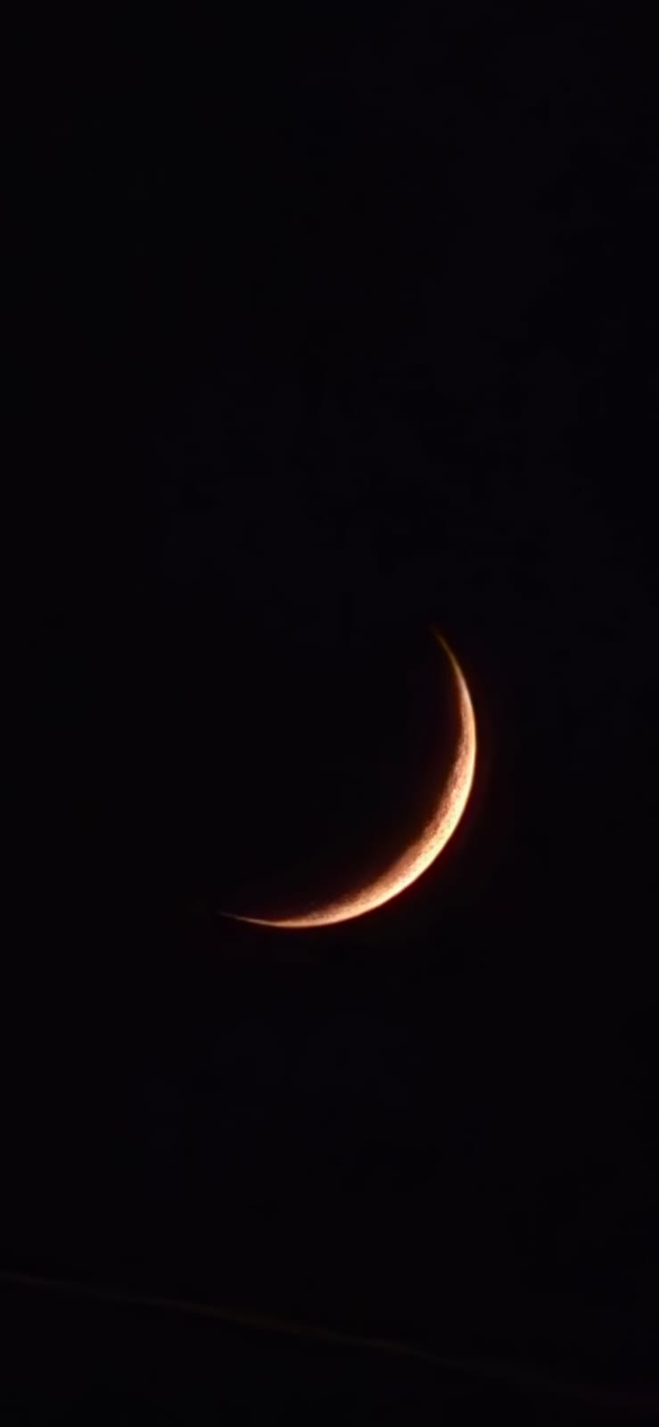 A narrow crescent moon shining in a black sky.